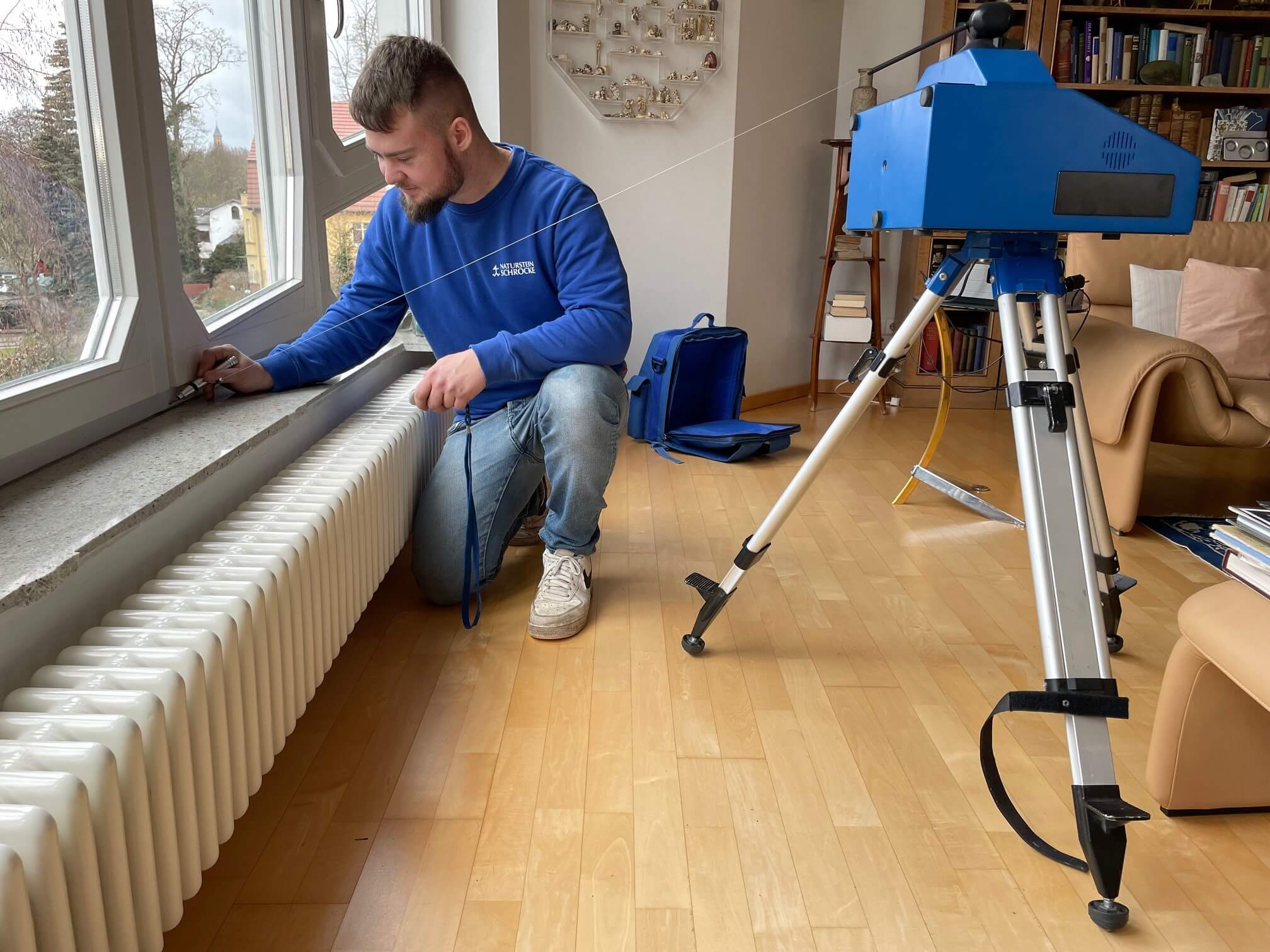 Mann misst Raum in Berlin mit Gerät, Vorbereitung zur Montage von Arbeitsplatten aus Naturstein, helles Zimmer, Holzboden.