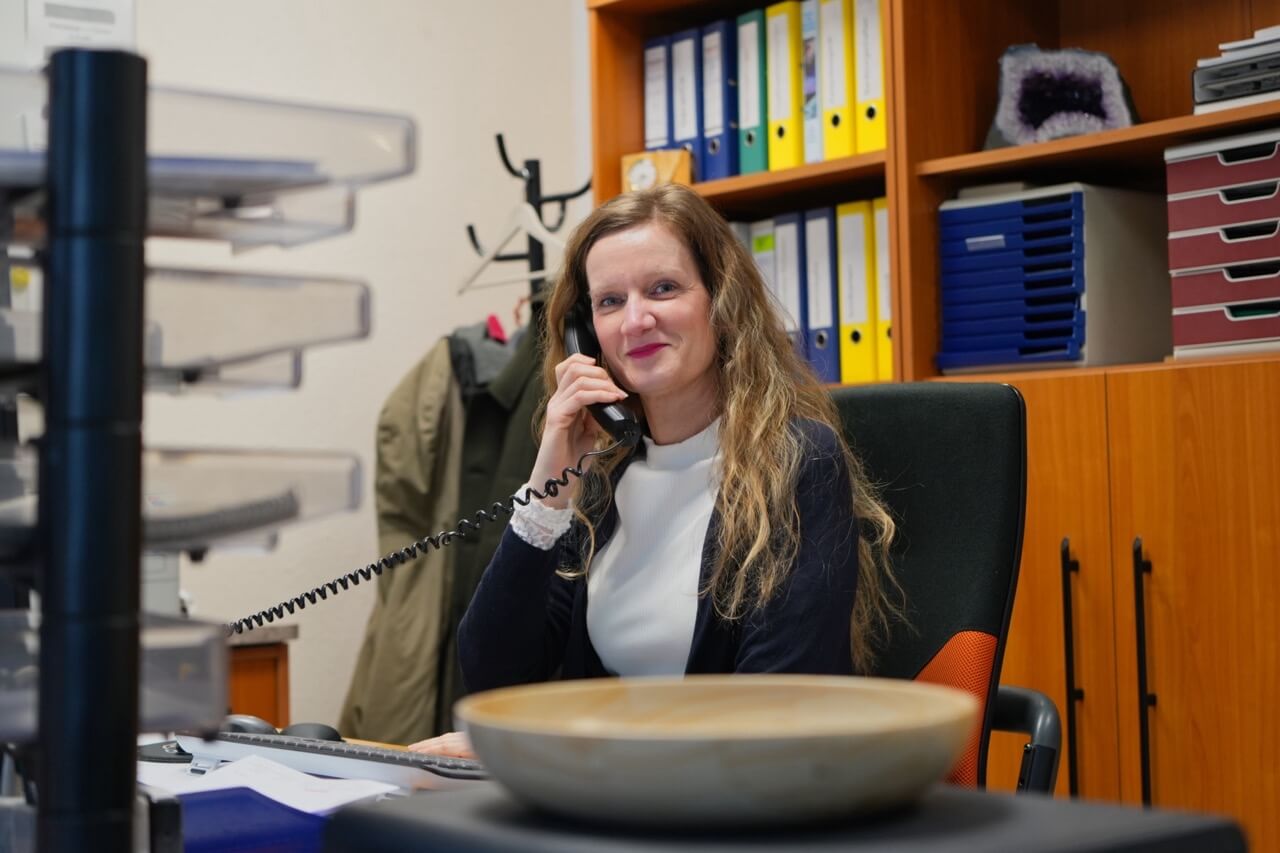 Freundliche Beraterin am Schreibtisch hilft am Telefon bei der Auswahl von Arbeitsplatten aus Naturstein für Projekte in Berlin.