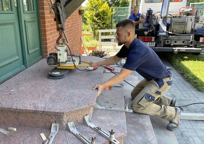 Arbeitsplatten aus Naturstein werden mit einem Hebegerät auf Außentreppen vor einem Backsteingebäude in Berlin montiert.